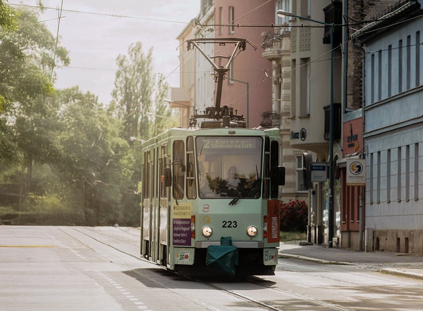 Starßenbahn von vorne mit Häuserzeile und Park